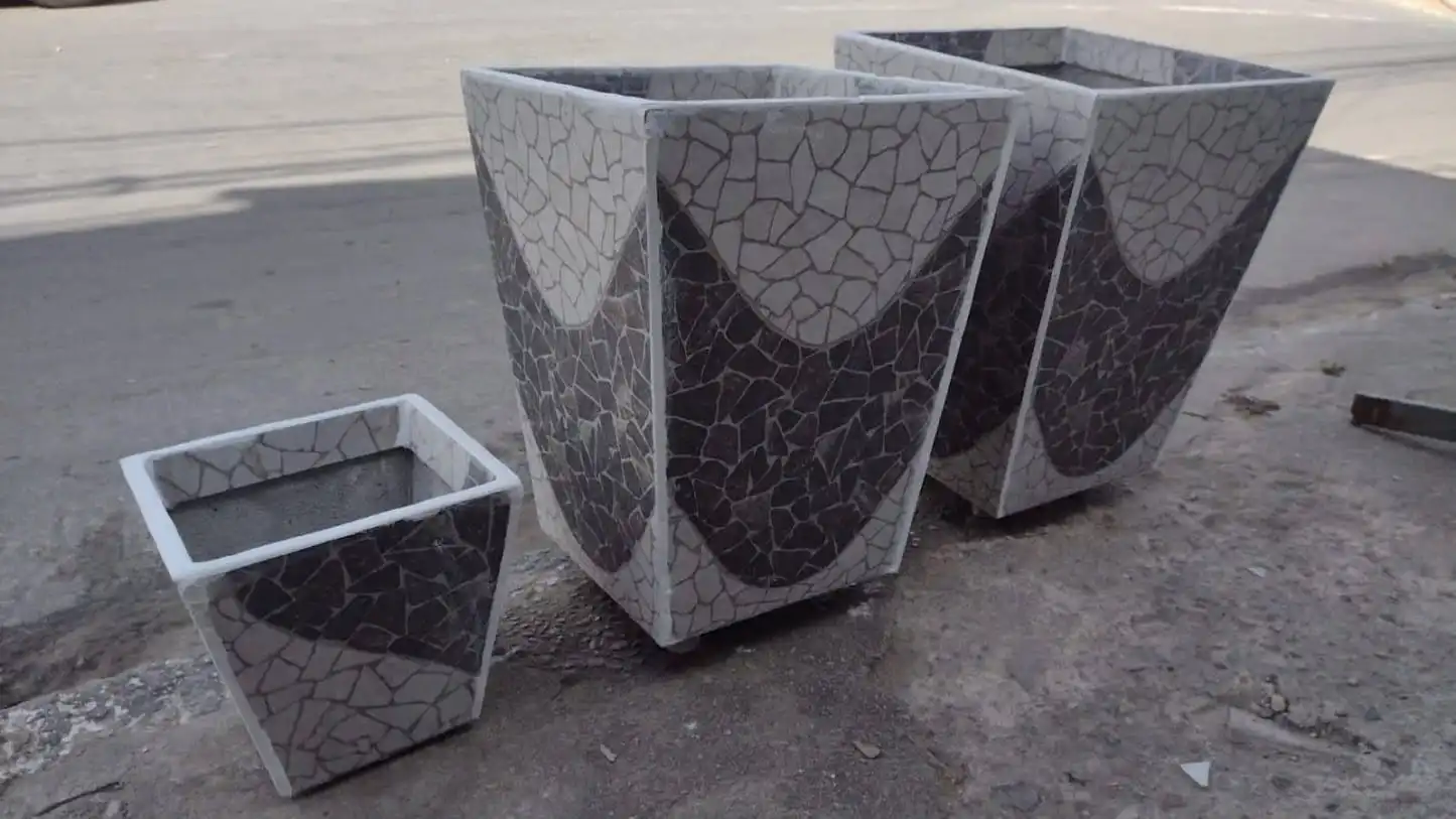 Mãos de artesão montando peças de mosaico em um vaso de concreto